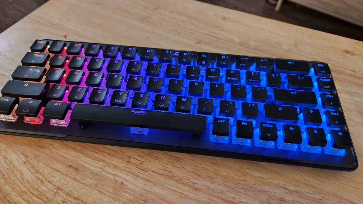 Black Roccat Vulcan II Mini Air keyboard with colorful LED backlit display resting on top of wooden surface.