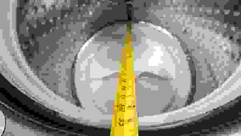 Yellow measuring tape being used to measure the depth inside of the washing machine drum.
