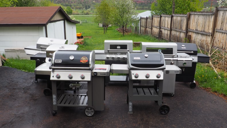 Seven gas grilled set up beside each other in a backyard.