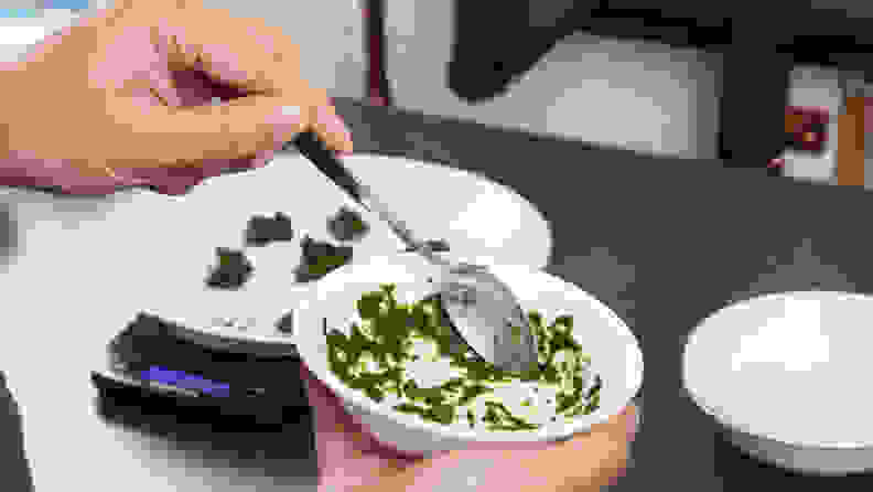 A hand moves a spoon around a dirty bowl, spreading a spinach stain around uniformly.