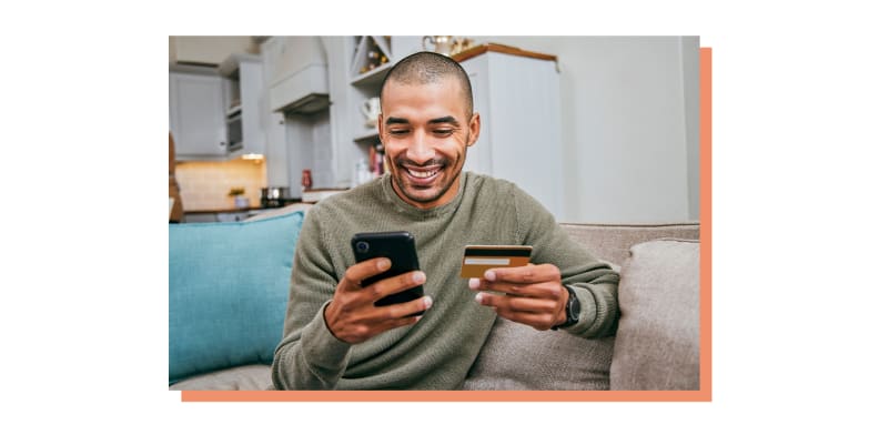 Person holding credit card and cell phone while smiling.