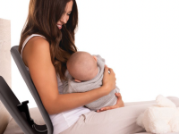 A mother smiles at her baby as they sit on a bed using the Ready Rocker.