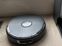 Black Narwal vacuum and docking station on a tan floor.