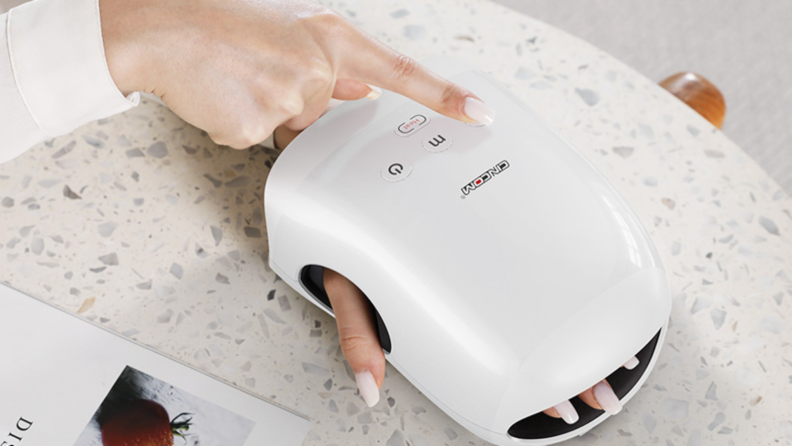 A hand is inserted in a Cincom hand massager machine, while the model's other hand presses the controls on top of the machine.