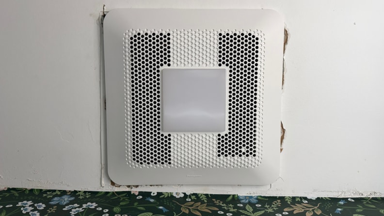 An exhaust fan on a ceiling next to a green floral wall