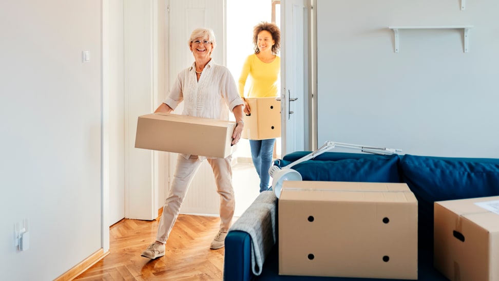 Two people holding boxes move into a new apartment.