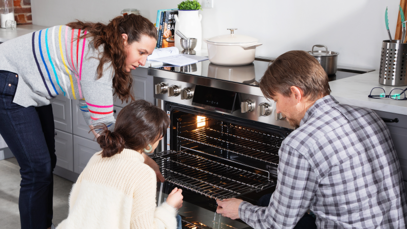 Three people crouch in front of an open oven.