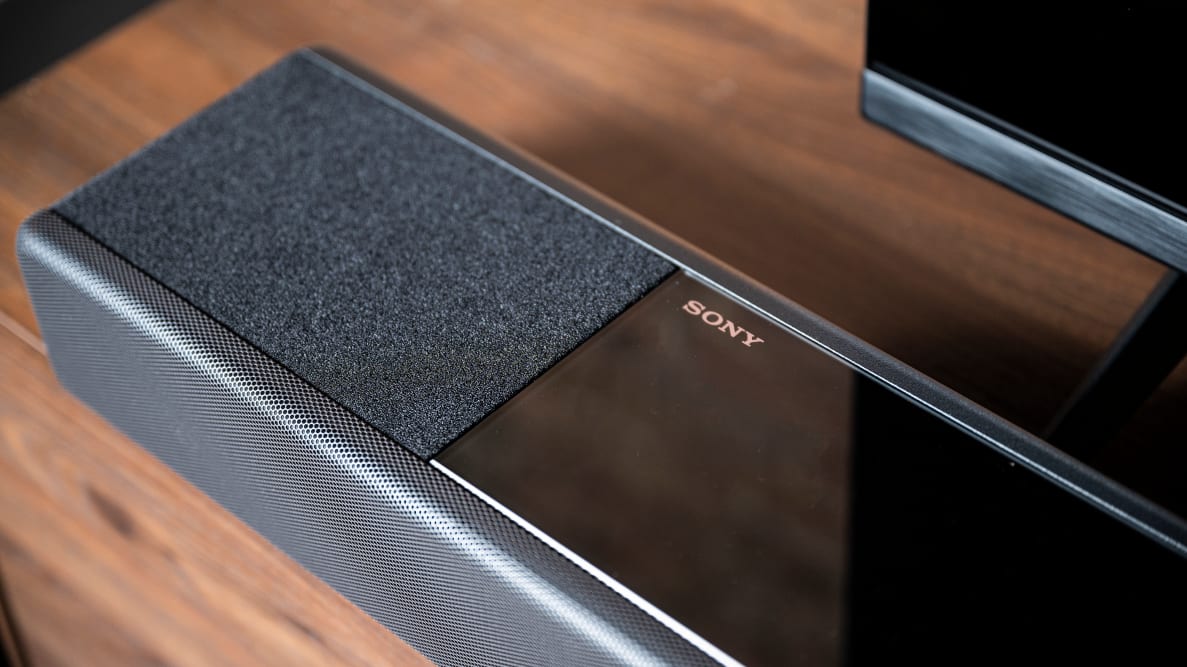 Sony's all-black slab of sound sits on a wooden table, a silver Sony logo glimmering in the center left on a glass panel next to its upfiring driver covered in acoustic fabric.