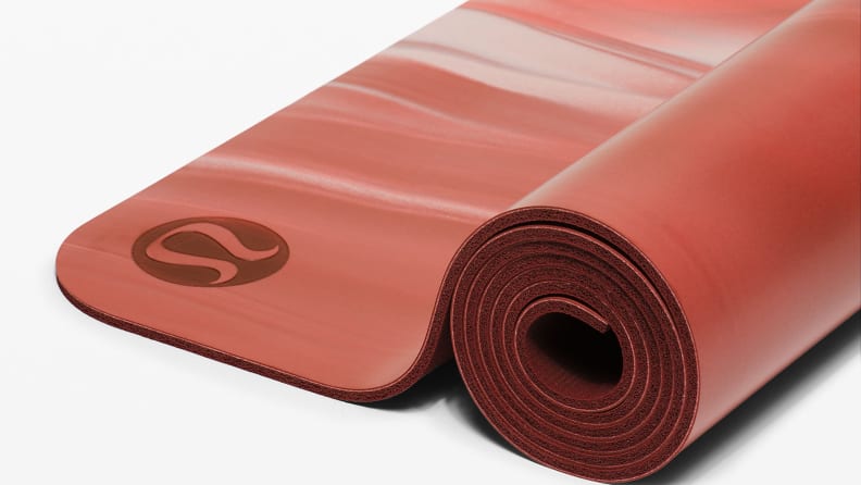 Red colored exercise mat rolled up on white background.