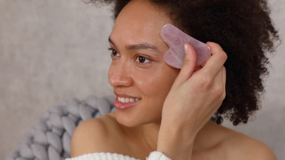 A woman using a gua sha stone to smooth her forehead.