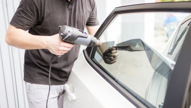 A person is using a heat gun to remove a decal from the inside of a car window.