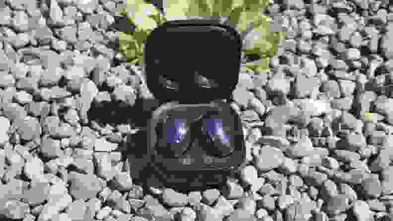 An open Samsung Galaxy buds case on gravel.