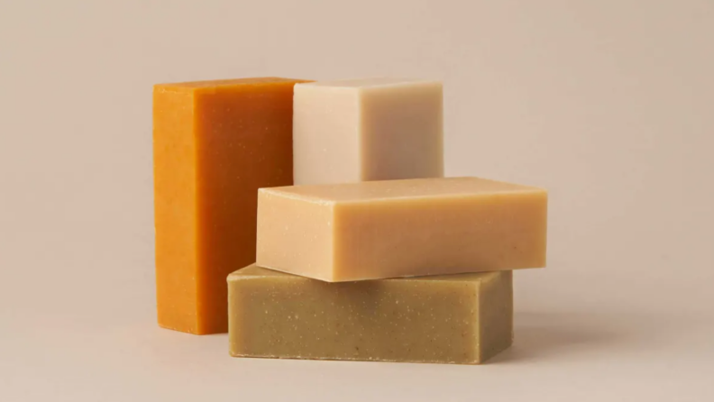 Three neutral colored By Humankind shampoo bars stacks on top of each other with an orange one standing to the left of the stack.