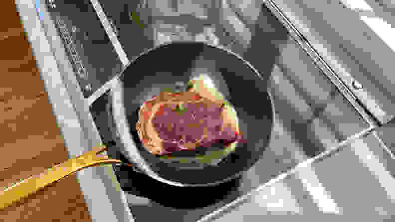 The Frök frying pan, with a piece of ribeye steak and some garlic inside, is sitting on an induction cooktop.