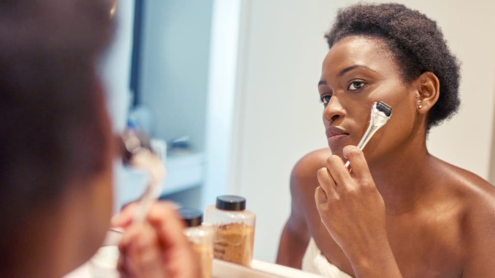 A woman looks into the mirror and holds a dermaroller up to her cheek.