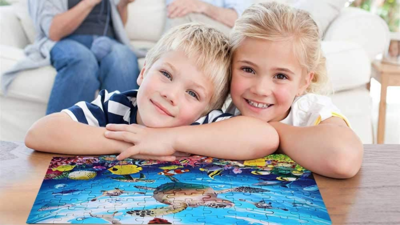 Two children lean against a completed turtle puzzle.