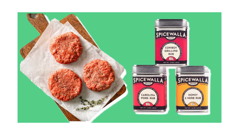 Raw burger patties on a tray, next to three containers of spices on a green background.
