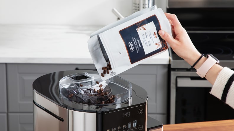 A person pouring coffee beans from a bag into the built-in conical burr grinder.