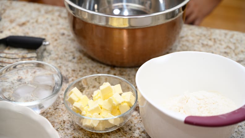 Pie ingredients like butter, flour, ice cold water, and salt in bowls on a countertop.