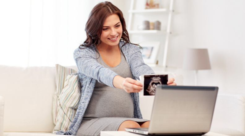 A mother-to-be holds up a sonogram picture to a laptop screen