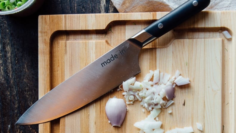 Chef's knife on a wooden cutting board with cut shallots.