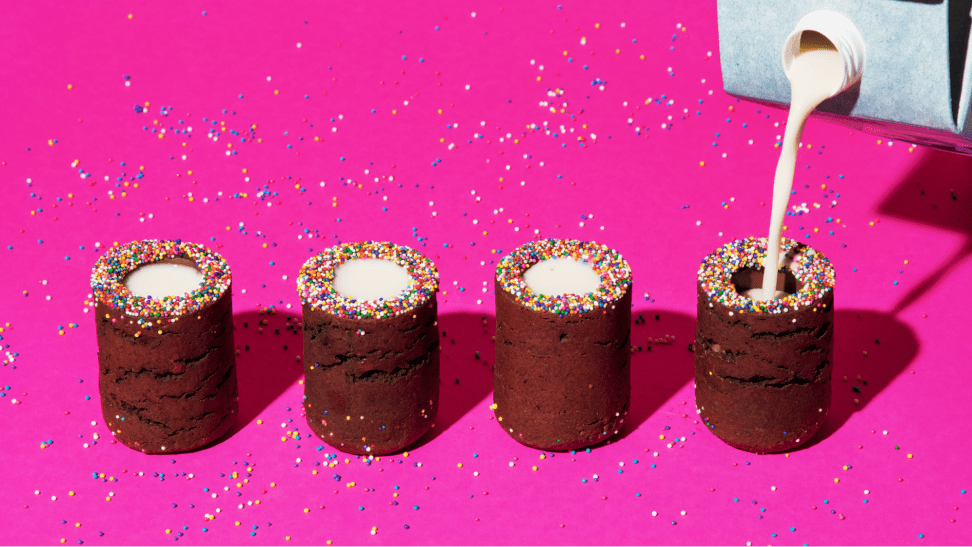 Milk being poured into cylindrical desserts on a neon pink background