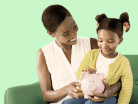 Small child sitting on child's lap while inserting money into pink porcelain piggy bank while sitting on couch.