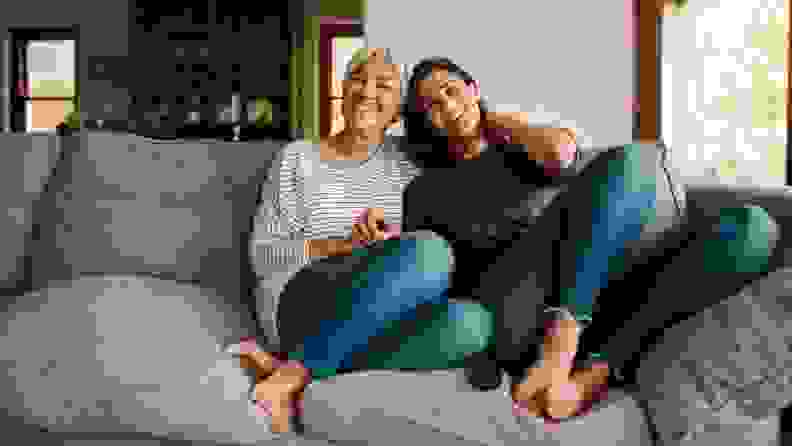 A pair of individuals (implied to be a parent and child) sit smiling on a couch.