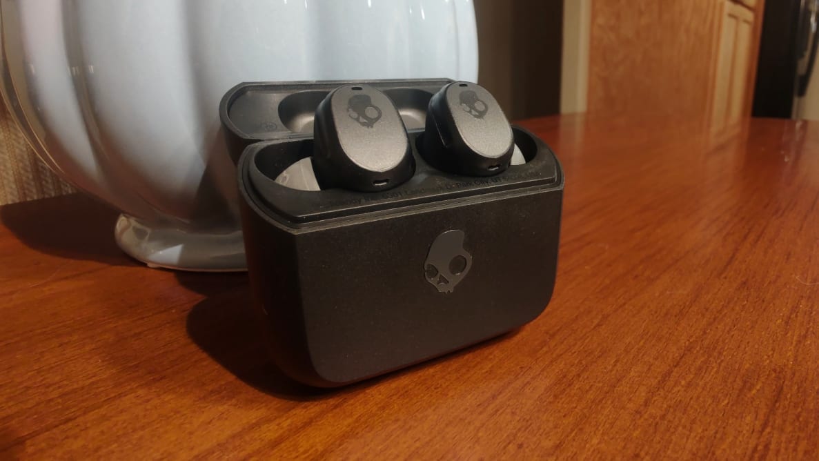 The oval and black Mod earbuds sit in their case on a wooden cabinet.