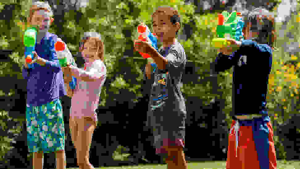 Four kids lined up outside shooting water guns and Nerf Super Soakers