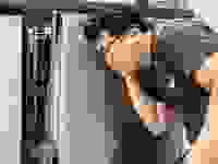 A person crouched down and listening closely to a dishwasher.
