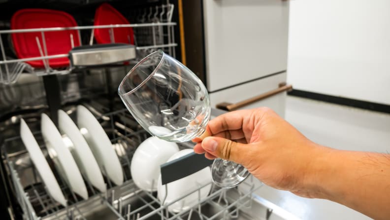 A person holding a clear wine glass in front of an open Bosch 800 Series SHP78CM5N dishwasher.