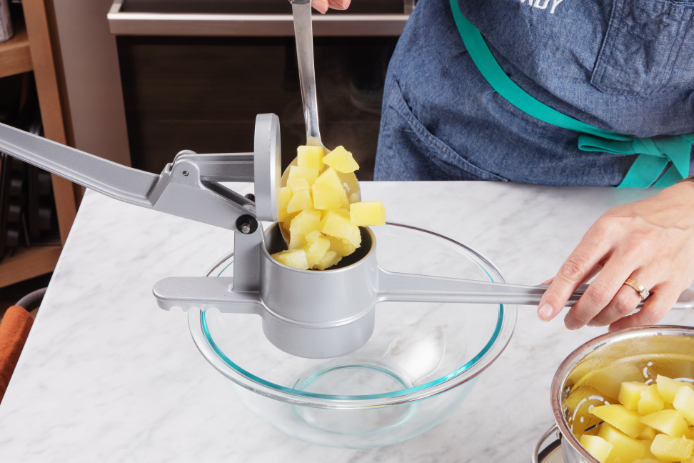 Cubed potatoes in a potato ricer over a glass bowl