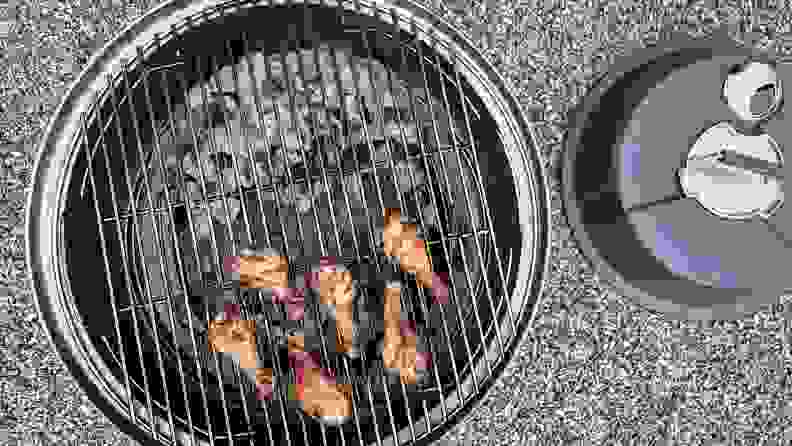 Chicken drumsticks cook on a grate over a charcoal grill.