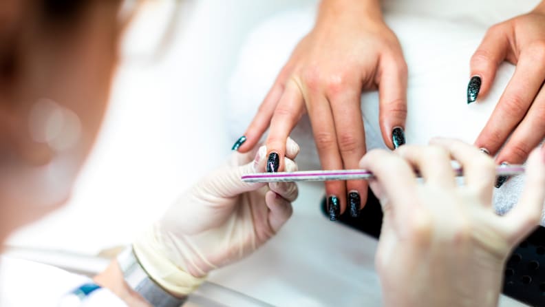 A closeup on a nail tech's hands working on someone's fingernails.