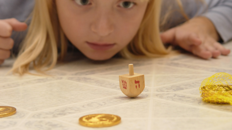 A young girl watches a dreidel spin.