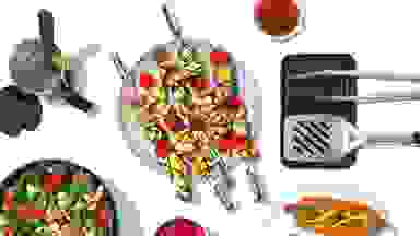 A top-down photo of grilled veggies, hotdogs, and the grilling tools used to good them.
