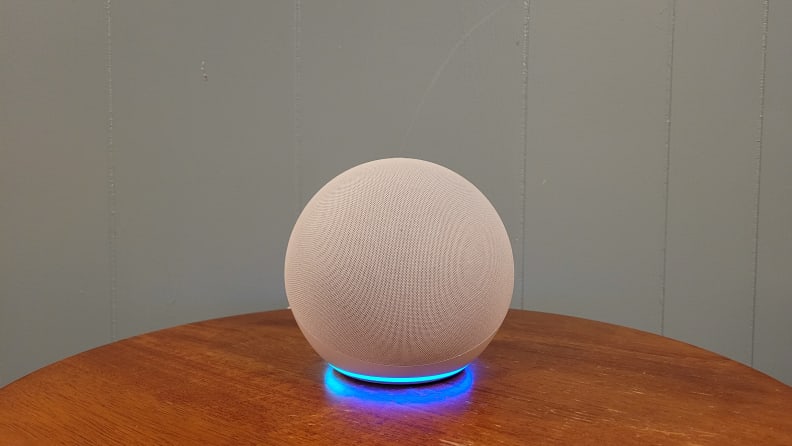 Product shot of the Amazon Echo smart speaker sitting on top of circular wooden table indoors.
