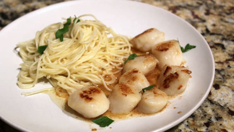 A white plate filled with scallops and pasta.