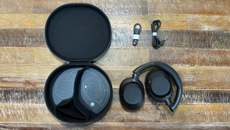 The Sony Ult Wear, its carrying case, and cables displayed on a wooden table.