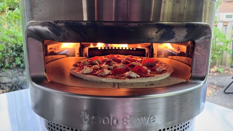 Small pepperoni pizza inside of Solo Stove Pizza Oven outdoors.