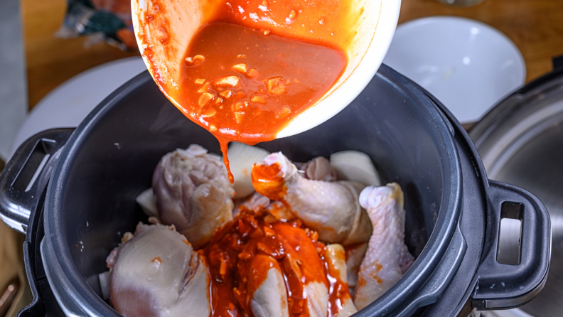 A bowl of sauce being poured over raw chicken in a slow cooker