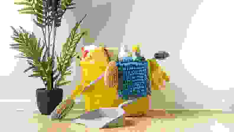 A yellow bucket of cleaning supplies to the right of a houseplant.