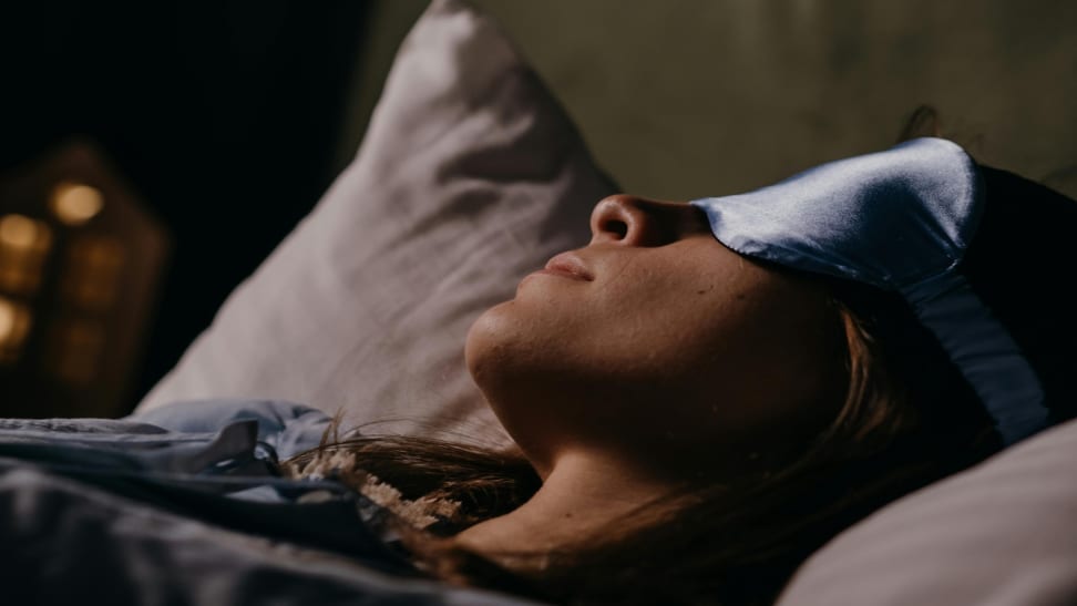 Woman sleeping on a bed wearing a blue silk sleeping mask.
