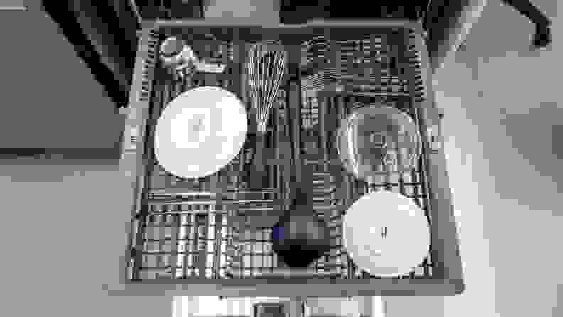 Upper rack within dishwasher with plates and assorted utensils inside.