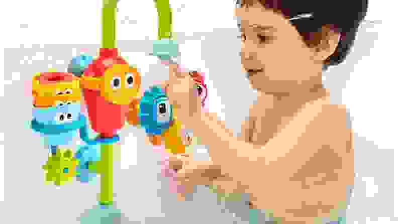 Toddler child plays with a vibrantly colored waterpark-style bath toy that suctions to the wall and sprays water.