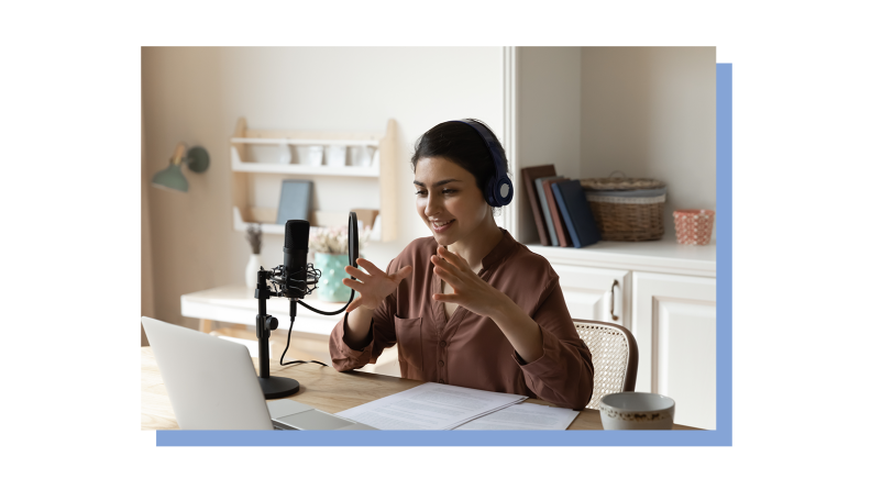 A podcaster speaks and gesticulates during a table with a microphone and laptop.