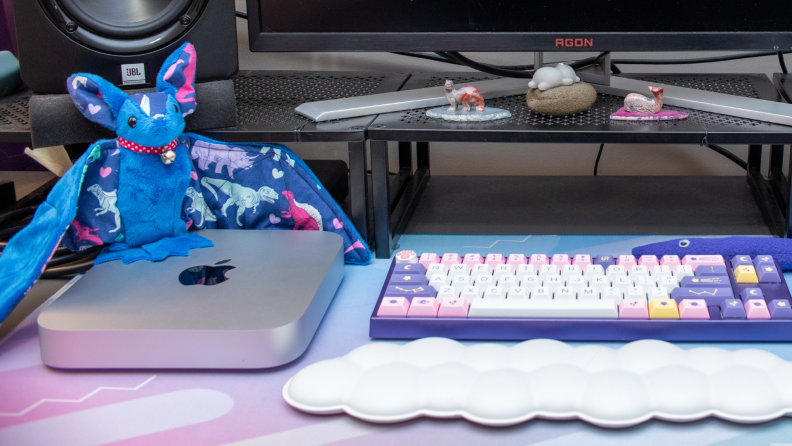 Apple Mac Mini next to desk set-up with colorful keyboard, plush stuffed animals, a desktop monitor and speaker.