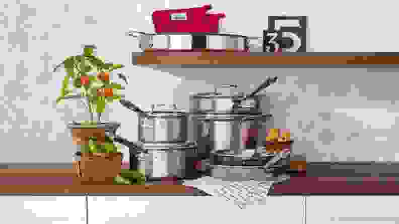 Several pots and pans are arranged neatly on a kitchen counter, along with some uncut peppers.