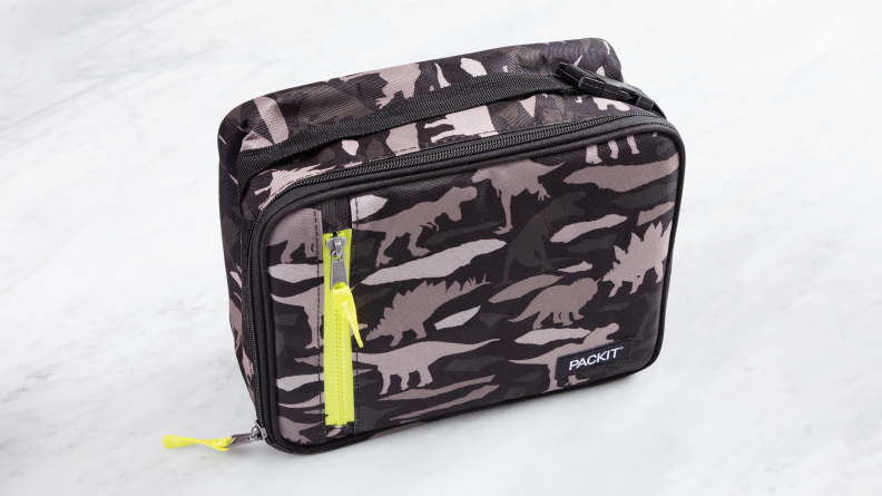The PackIt Freezable classic lunch carrier in dinosaur camo print sits closed on a marble counter.